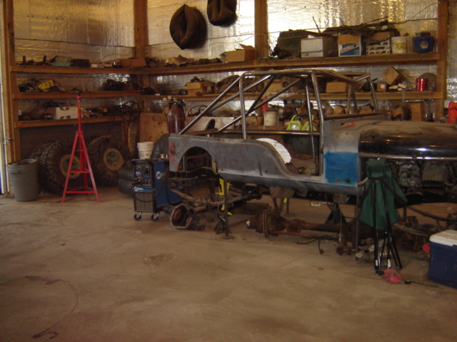 Jeep CJ-7 body and frame on jack stands in a workshop with tools and tires visible