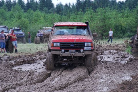 1989 Ford Bronco - Off-road vehicles, including a red 1989 Ford Bronco, tackle a muddy course during an event.