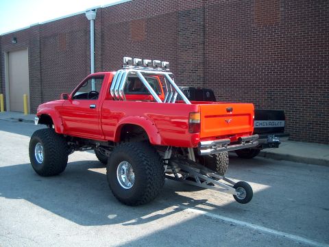 1978 Ford Bronco - A heavily modified red pickup truck is parked next to a black Chevrolet truck.