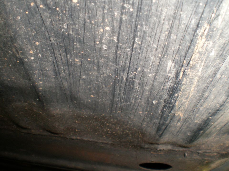 Underside of a vehicle showing wear and dirt. There's a circular opening visible