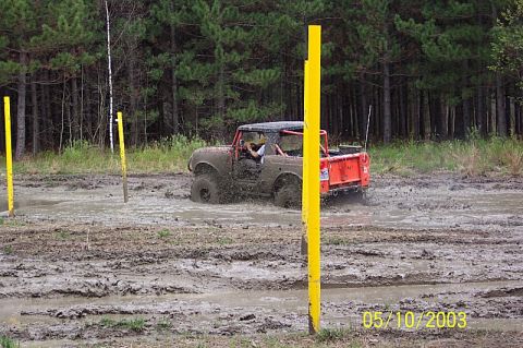 1978 Ford Bronco - Off-road vehicle navigating a muddy track with yellow poles marking the course.