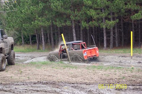 1978 Ford Bronco - An off-road vehicle navigates a muddy track, kicking up spray as it goes.