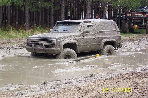 1978 Ford Bronco - A mud-caked Chevrolet K5 Blazer is partially submerged in a muddy puddle, with another vehicle visible in the background.