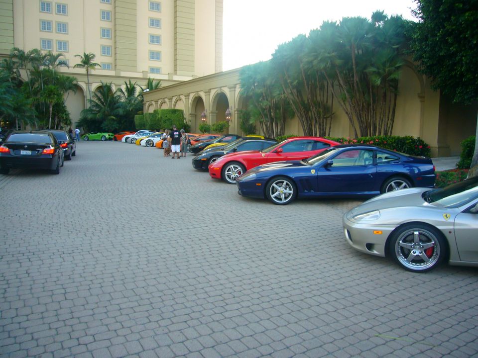 Silver Ferrari sports car front quarter view, parked on cobblestone with other cars and a building