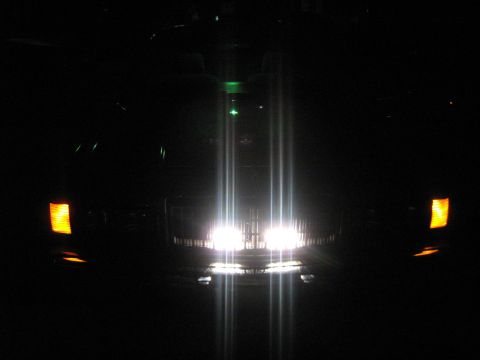 1988 Mercury Grand Marquis - Headlights and turn signals are illuminated on a dark vehicle, seen from the front at night.