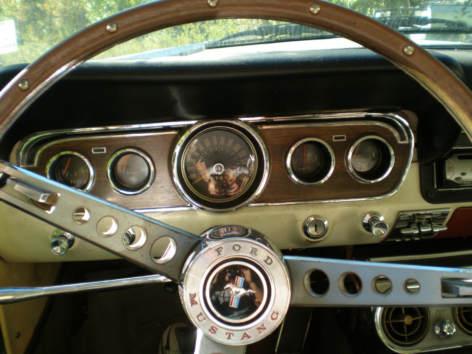 Close-up of a 1966 Ford Mustang interior, showing the steering wheel with the Mustang logo and the dashboard with gauges