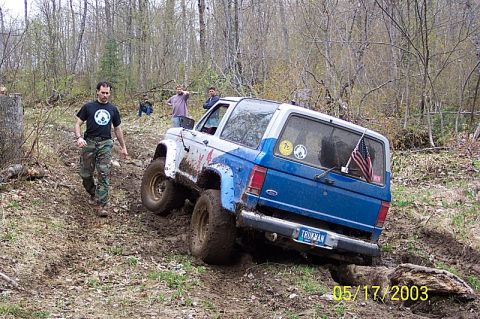 1978 Ford Bronco - A blue and white SUV navigates a challenging muddy off-road course.