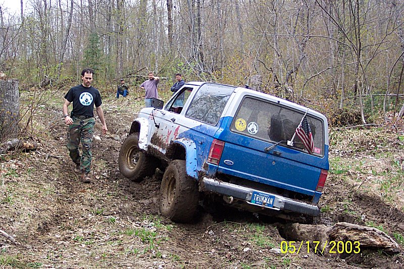 Blue and white SUV with "TRUMAN" license plate, tilted on muddy terrain