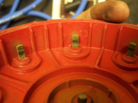 1995 Ford Bronco - A red distributor cap with metal terminals is held by a hand, with blue spark plug wires blurred in the background.