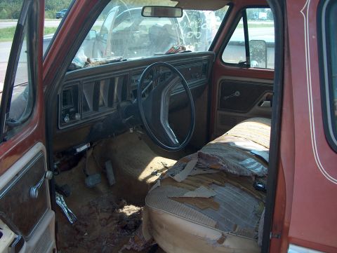 1979 Ford F-250 - The interior of an old truck shows a worn dashboard and a ripped seat, with debris on the floor.