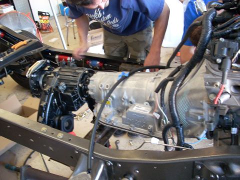 1992 Ford Bronco - Mechanics work on the drivetrain of a vehicle chassis, focusing on the transmission and transfer case assembly.