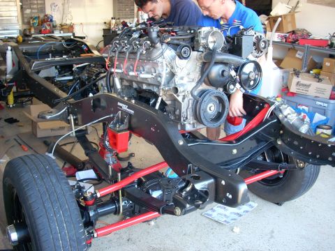 1992 Ford Bronco - Mechanics assemble an engine into a vehicle chassis in a garage setting.