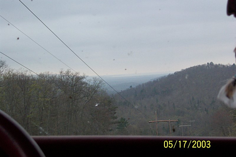 View from inside a vehicle looking out at a wooded hillside and sky. Date stamp 05/17/2003