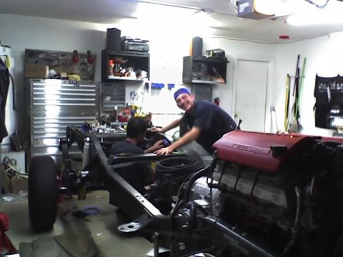 1992 Ford Bronco - Two men are actively working on the chassis and engine of a vehicle inside a garage setting.