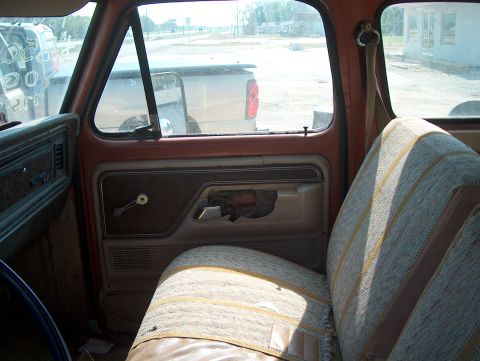 1979 Ford F-250 - The interior of a truck cab shows a worn seat and a damaged door panel, with another vehicle visible outside.
