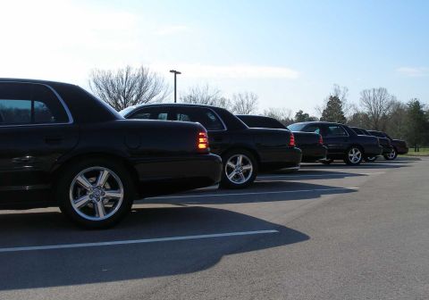 2001 Ford Crown Victoria - A row of black Ford Crown Victoria sedans are parked in an outdoor lot under a clear sky.
