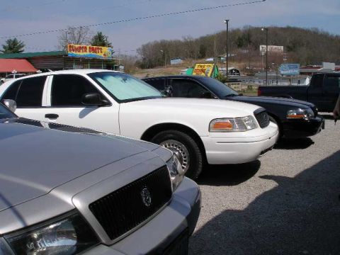 2001 Ford Crown Victoria - A white 2001 Ford Crown Victoria is seen from the front-three-quarter view, parked alongside other vehicles.