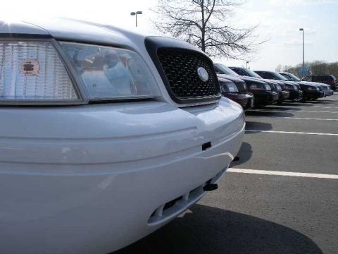 2001 Ford Crown Victoria - Close-up of a white 2001 Ford Crown Victoria's front end, with a line of similar vehicles in the background.