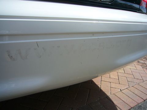 2001 Ford Crown Victoria - A close-up of a white car's rear bumper shows faint text, possibly a website, on its surface.