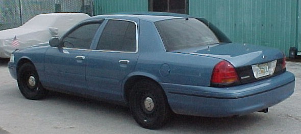 Light blue Ford Crown Victoria sedan seen from rear-left with black steel wheels.