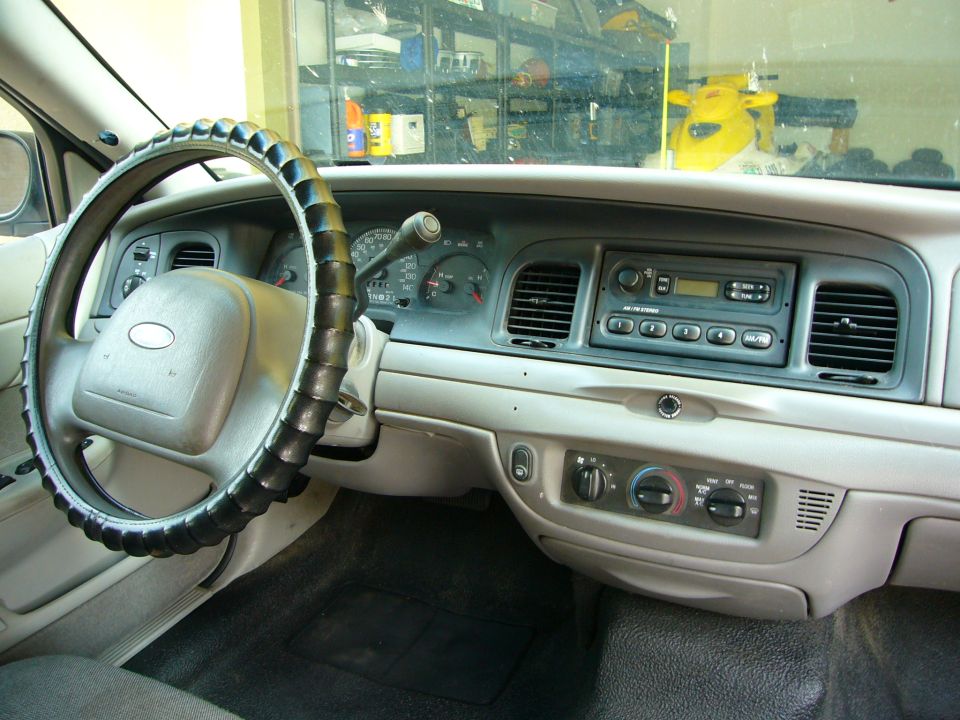 Dashboard of a 2001 Ford Crown Victoria with a black steering wheel cover, showing the radio and climate controls