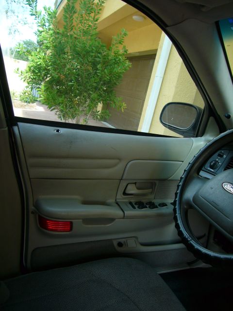 2001 Ford Crown Victoria - The interior of a Ford Crown Victoria shows the door panel, steering wheel, and a glimpse of the outside through the window.