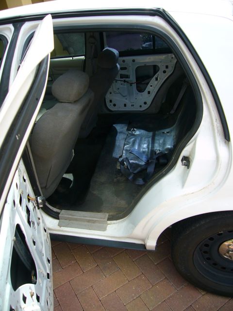 2001 Ford Crown Victoria - The interior of a white 2001 Ford Crown Victoria is visible with both rear doors open, revealing stripped door panels and exposed interior…