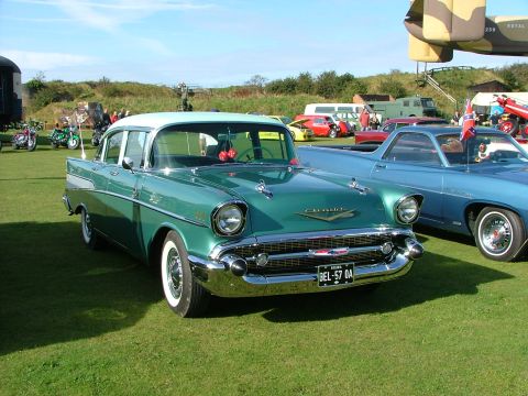 1988 Ford Sport - A classic green and white 1957 Chevrolet sedan is parked on a grassy field next to other vehicles.