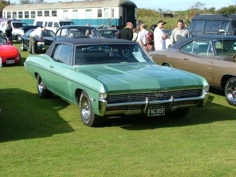 1988 Ford Sport - This green 1968 Chevrolet Impala SS coupe is displayed on a grassy field with other vehicles and a train car in the background.