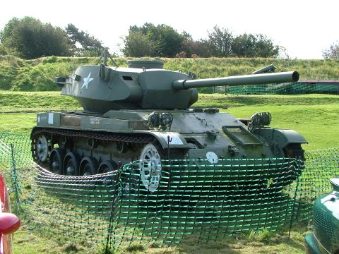 1988 Ford Sport - A military tank sits on display in a grassy field, partially obscured by a protective fence.