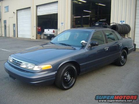 1996 Ford Crown Victoria - A dark blue Ford Crown Victoria is parked in front of a commercial building with its doors closed.