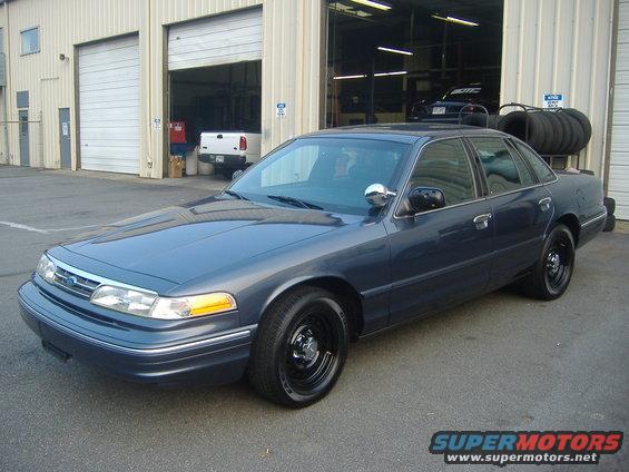 Dark blue Ford Crown Victoria parked outside a garage with a white pickup truck visible inside