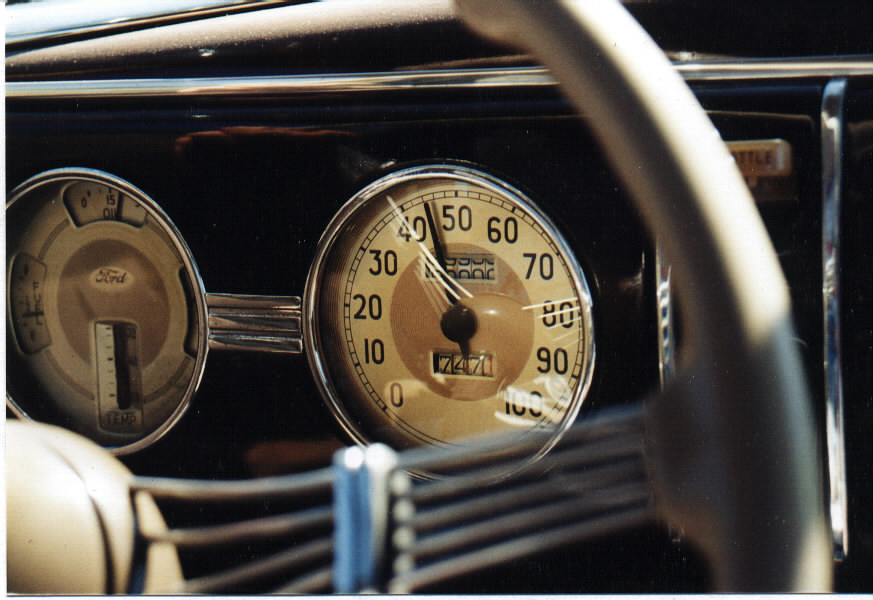 Close-up of vintage Ford speedometer reading 7471 miles beside a Ford combination gauge on a dark dash
