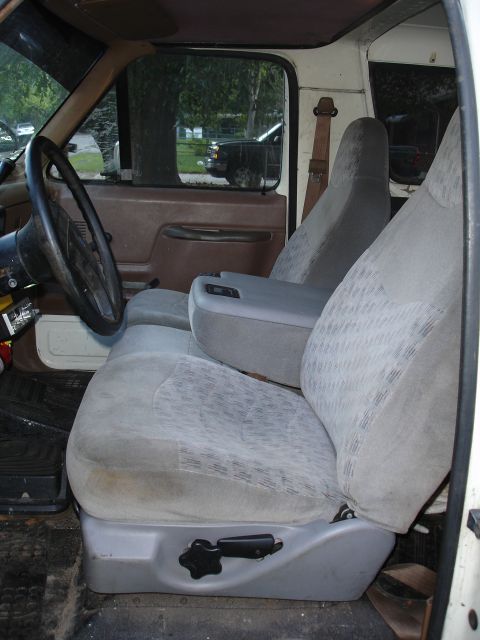 1989 Ford Bronco - The interior of a truck shows the driver's side seat, armrest, and steering wheel, with a view of the outdoors through the window.