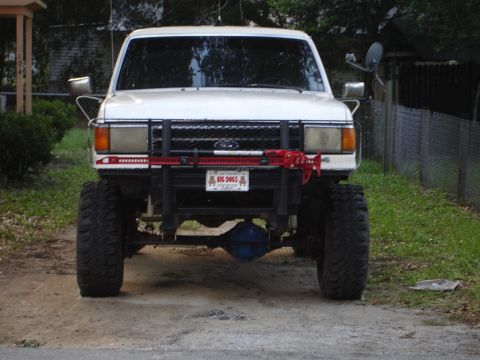 1989 Ford Bronco - This lifted Ford Bronco features oversized tires and a prominent red Hi-Lift jack on its front bumper.