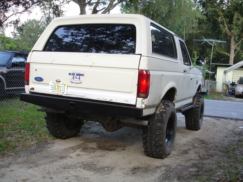 White Ford Bronco lifted with big tires, rear view. Has a 'Blue Ridge 4x4' sticker and Florida plates