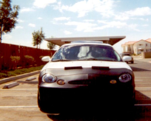 Front view of white sedan with black front-end bra in a parking lot