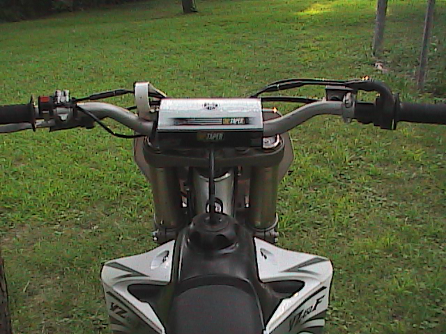 Rider POV over a dirt bike's ProTaper bars and forks toward a grassy yard