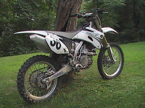 2007 Yamaha YZ450F - A white 2007 Yamaha YZ450F dirt bike is parked next to a tree, showing its side profile with the number 36 visible.