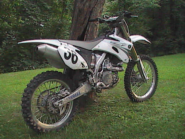 White Yamaha motocross dirt bike with number 56 plates leaning against a tree on grass
