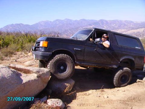 1990 Ford Bronco - Driver navigates a black 1990 Ford Bronco over challenging rocks during an off-road excursion.
