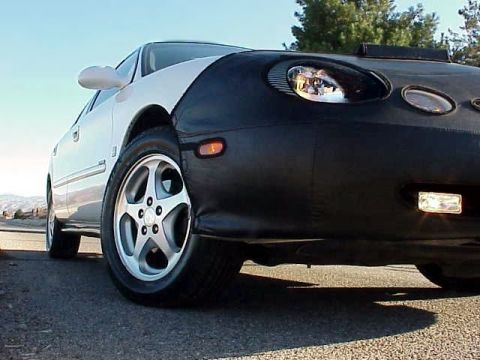 1999 Ford Taurus - A car is parked on a road, its front end covered by a black bra, revealing the headlights and a side marker light.