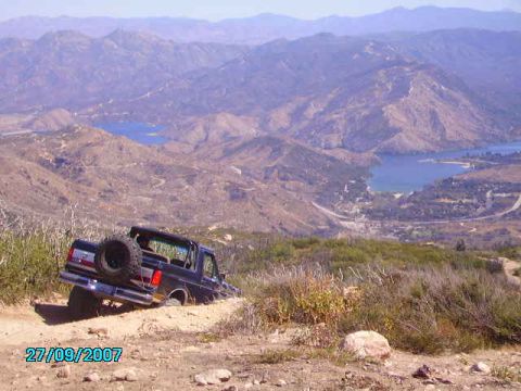 1990 Ford Bronco - A 1990 Ford Bronco tackles a challenging off-road trail with a scenic mountain and lake vista in the background.