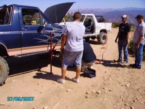 1990 Ford Bronco - A group of people appear to be working on a blue Ford Bronco with flame decals, with a white pickup truck in the background.
