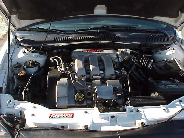 1999 Ford Taurus engine bay with a Flowmaster sticker and Supermotors.net watermark