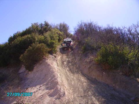 1990 Ford Bronco - A vehicle navigates a challenging off-road path under a clear blue sky.