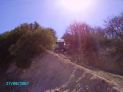 1990 Ford Bronco - A white SUV navigates a steep dirt path surrounded by dry brush and trees under a bright blue sky.