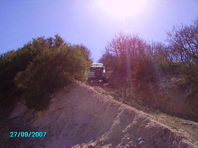 White SUV driving up a dirt hill, seen from below and behind
