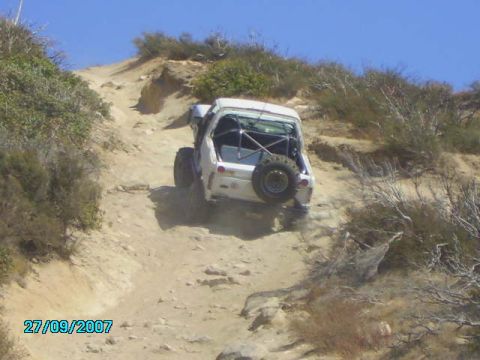 1990 Ford Bronco - A white off-road vehicle navigates a steep, rocky dirt path under a clear blue sky.