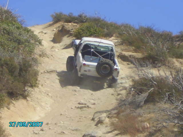 White off-road vehicle with roll cage and spare tire on the back, driving on a dirt trail